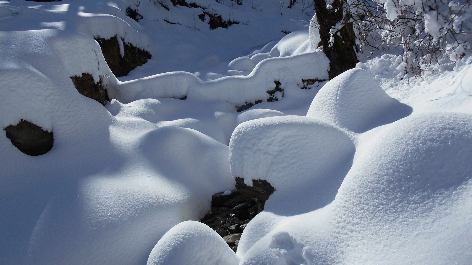 Fresh snow piled over boulders beside the Kedarkantha trail