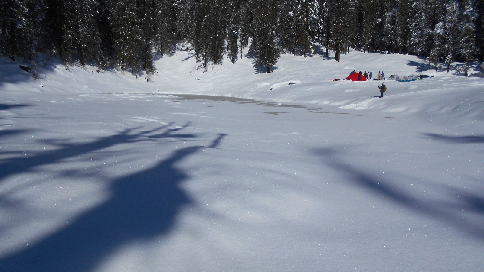 A snowfield with a campsite at its edge on the Kedarkantha trek